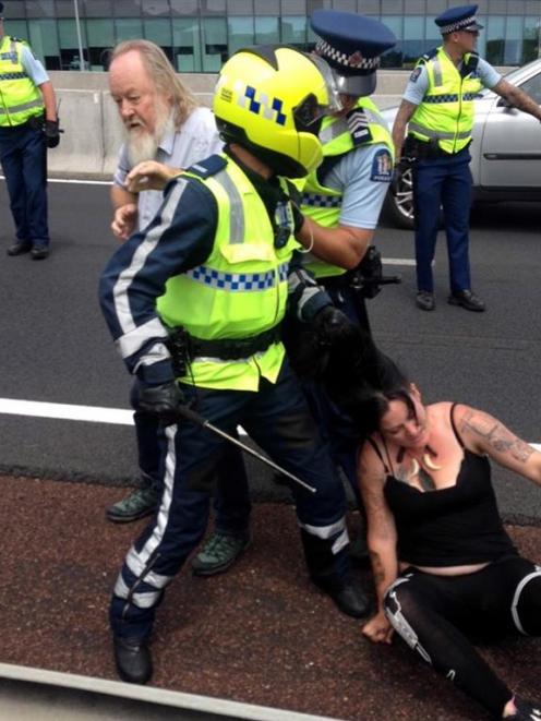 A police officer (in helmet) grabs Dunedin anti-TPP protester Olive McRae by the hair as she is...