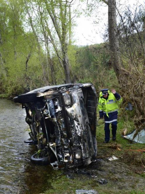 A police officer inspects the burnt wreckage of a van, which ended up in Silver Stream near...