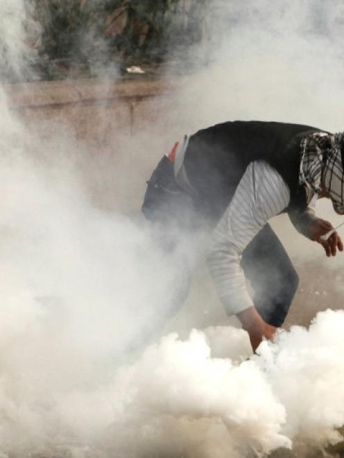 A protester against Egypt's President Mohamed Mursi tries to pick up a tear gas canister fired by...