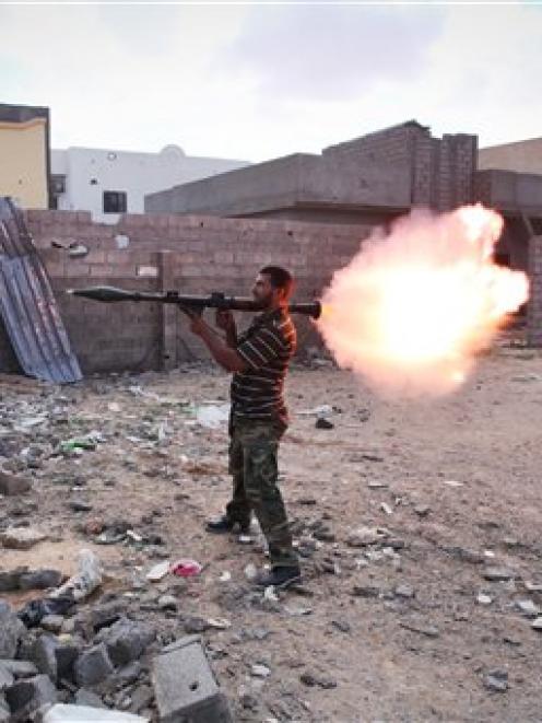 A revolutionary fighter fires a rocket-propelled grenade at Gaddafi loyalists in downtown Sirte,...