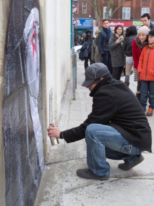 A street artist pastes an image on a London wall from which a section, containing an image...
