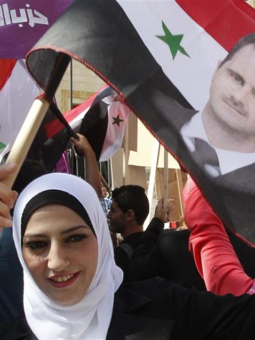 A supporter of Syria's President Bashar al-Assad waves a Syrian national flag depicting Assad's...