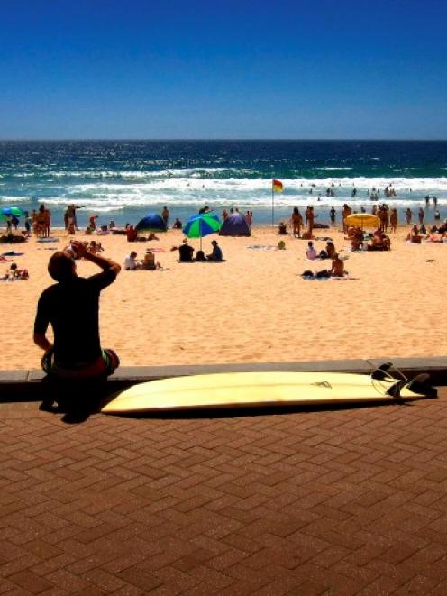 A surfer sits with his surfboard on the footpath above Manly Beach as the temperature rises in...