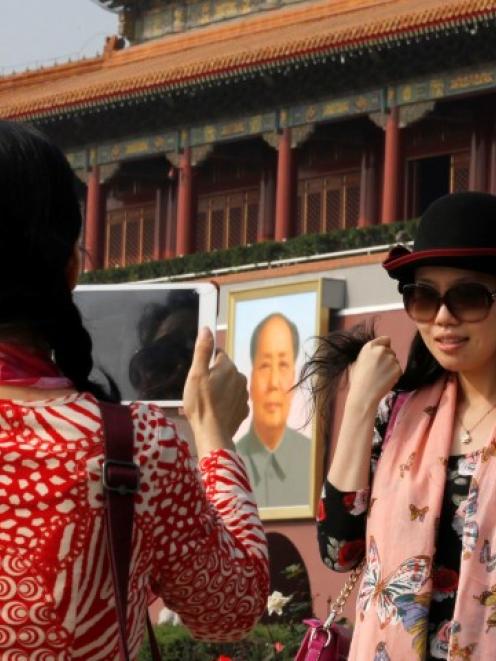 A tourist poses for a photograph in front of the giant portrait of late Chinese Chairman Mao...
