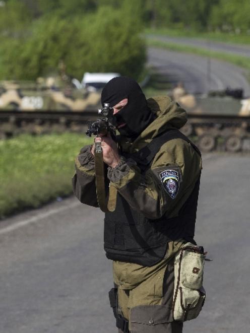 A Ukrainian soldier, with armoured personnel carriers behind him, points his weapon at an...