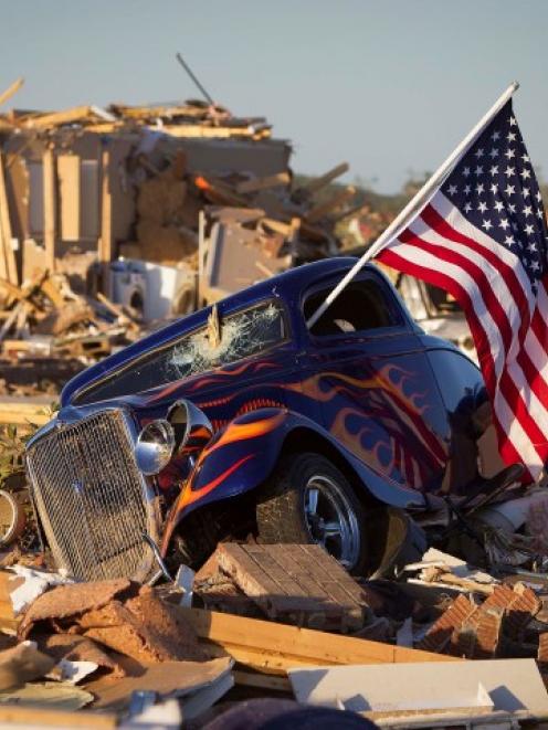 A US flag sticks out the window of a damaged hot rod in a suburban area after a tornado near...