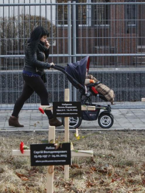 A woman with a child walks past crosses with the names of victims who were killed in the shelling...