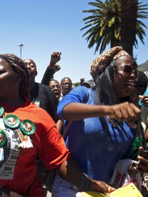 A woman with a Nelson Mandela t-shirt and badges sings and dances along with others in front of...