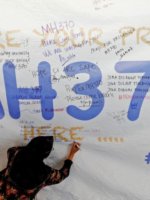 A woman writes a message of support and hope for the passengers of the missing flight on a banner...