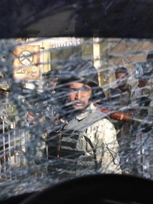 An Afghan soldier passes by the shattered window of a destroyed police car after an explosive...