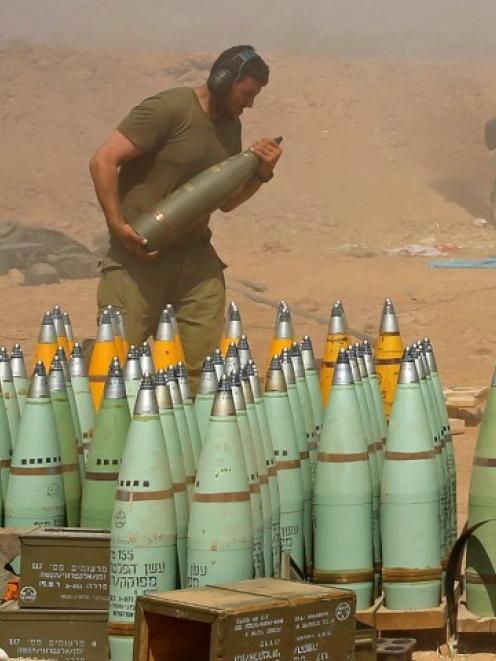 An Israeli soldier carries a shell at a mobile artillery unit while it fires towards the Gaza...