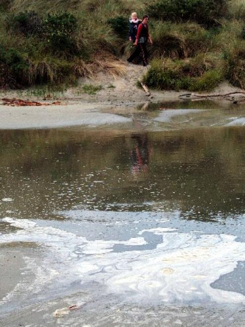 An unidentified woman carrying a baby walks close to the potentially toxic scum that has been...