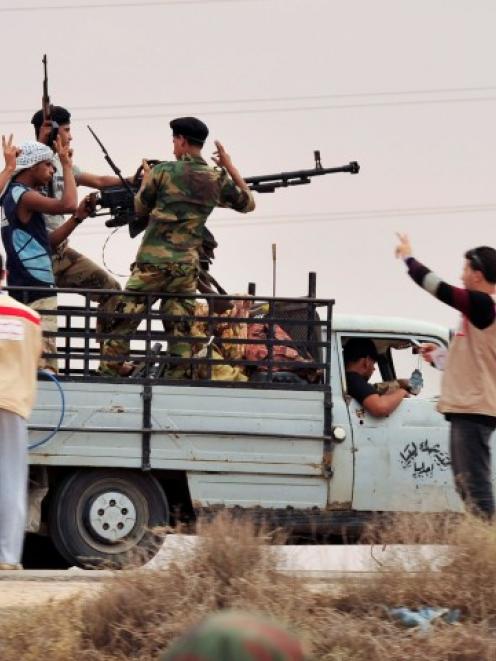 Anti-Gaddafi fighters flash victory signs behind an anti-aircraft gun as they take up position...