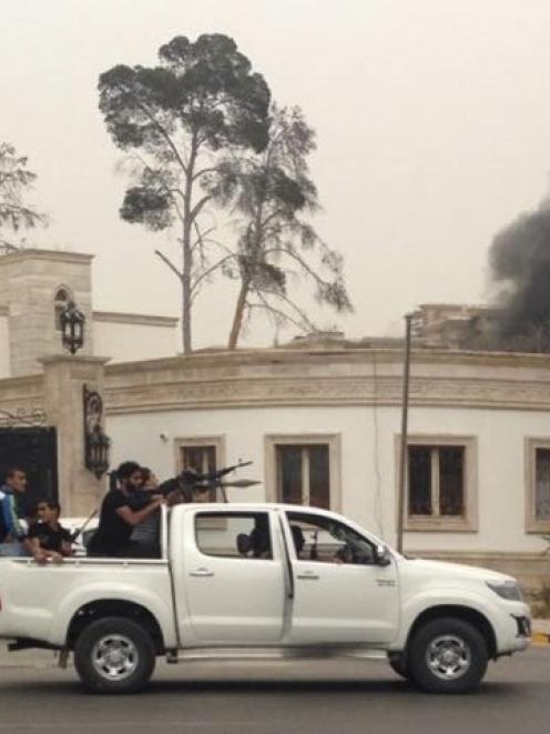 Armed men aim their weapons from a vehicle as smoke rises near the General National Congress in...