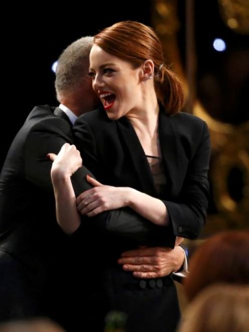 Birdman actress Emma Stone is hugged by Michael Keaton as they head to the stage to accept the...
