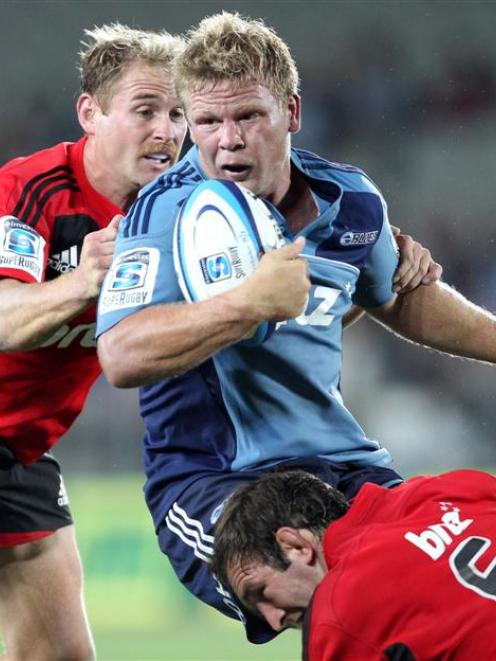 Blues loose forward Daniel Braid is tackled by Crusaders Andy Ellis, left, and George Whitelock....