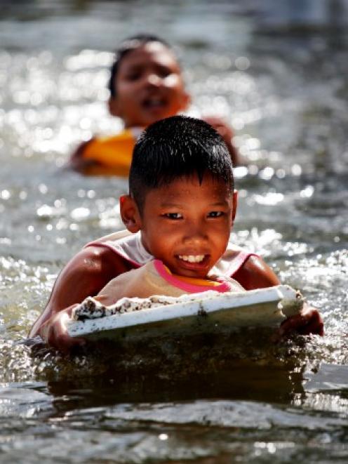 Boys play in the water in a flooded slum as floods advance into central Bangkok yesterday. The...