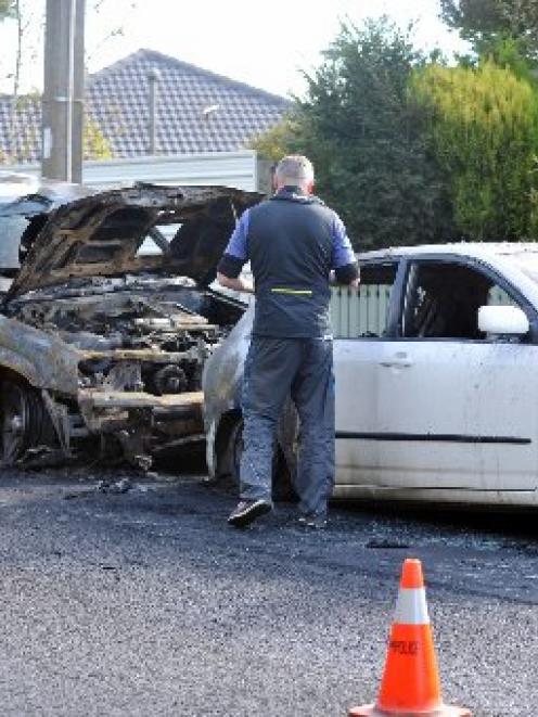 A Dunedin police photographer records the damage to two vehicles whose interiors were burned out...