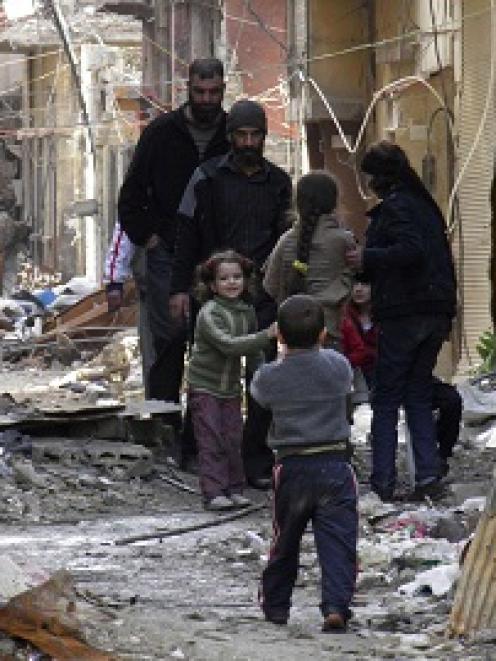 Civilians stand along a street amid garbage and rubble of damaged buildings in the besieged area...
