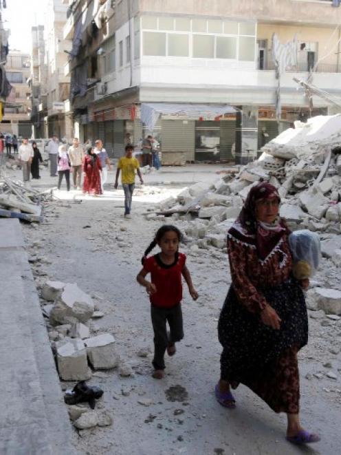 Civilians walk near a destroyed building after a Syrian Air Force fighter jet launched a bomb in...