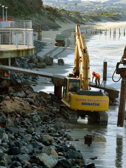 Contractors take advantage of low tide yesterday to continue piling rocks against the bottom of...