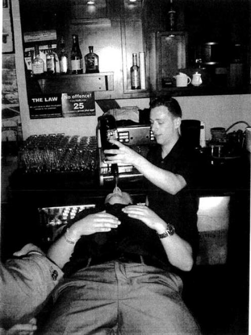 Craft Bar duty manager Michael Campbell pours liqueur from a  bottle into the mouth of a patron,...