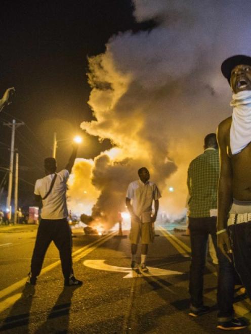 Demonstrators stand in the middle of West Florissant as they react to tear gas fired by police...