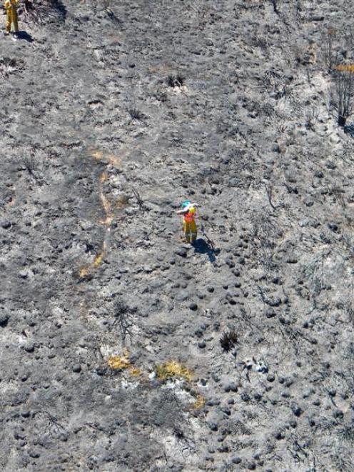 Department of Conservation fire crew members on the blackened face along the East Matukituki...