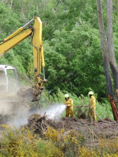 Fire crews and an excavator operator douse the Ettrick fire in scrub along the Clutha riverbank...