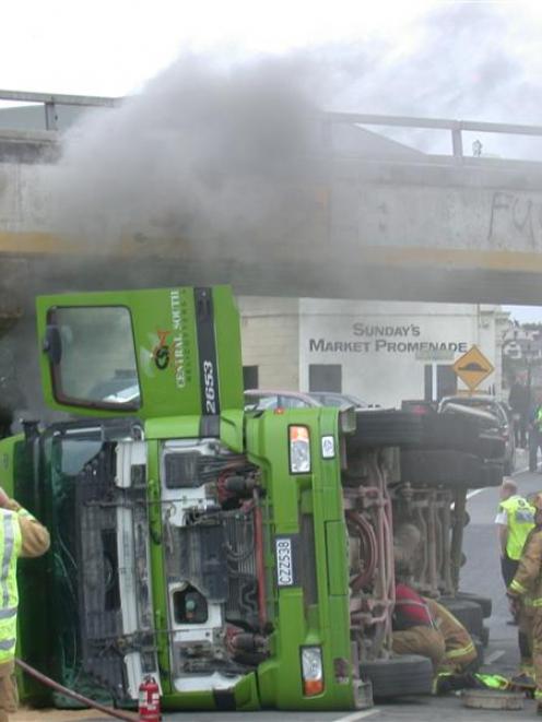 Firefighters work to turn off the engine of a truck that tipped over on to a car after a...