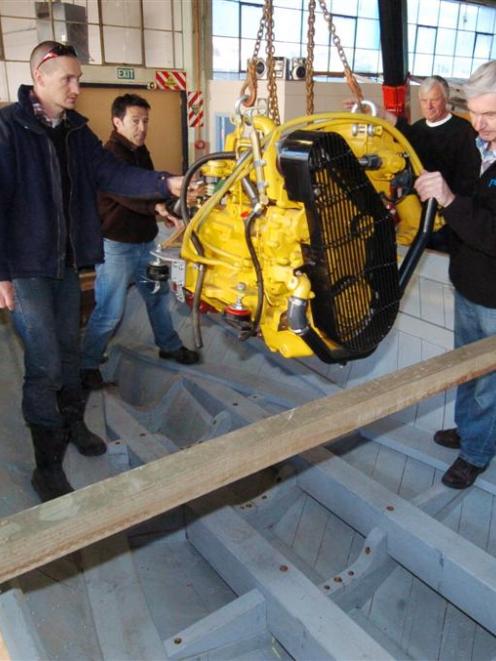 Guiding the new diesel engine into the hull of Elsie Evans yesterday are (from left) Scott Broere...