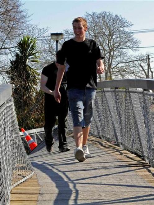 Ignoring warning tape closing a badly twisted footbridge over the Avon River, two boys cross to...