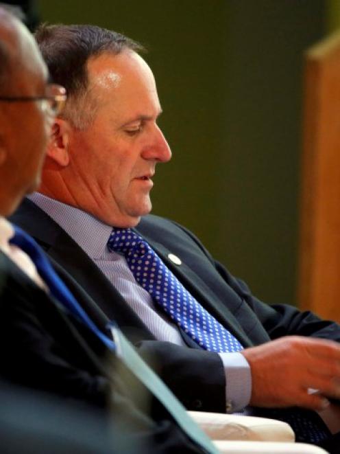 John Key (C) reads a document as he attends the opening session of the World Climate Change...