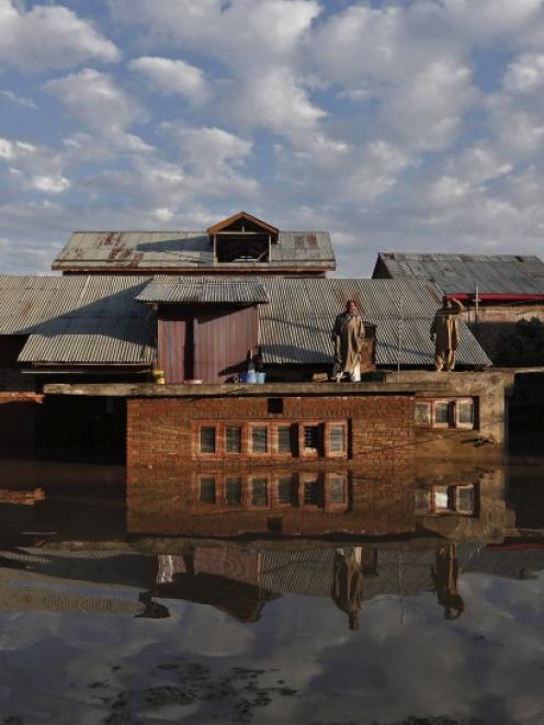 Kashmiri men stand on the roof of their flooded house as they wait to be rescued by Indian army...