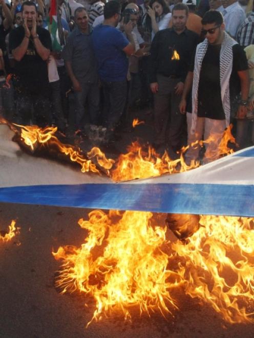 Lebanese and Palestinian protesters burn an Israeli flag during a demonstration to denounce...