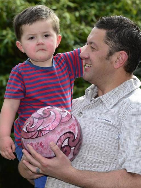 Manuaitu Haggie (2) at home with his father, Reihana, and the carved bowling ball up for auction....