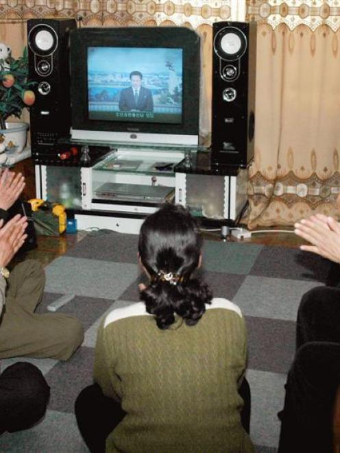 Members of a North Korean family clap as they watch an official announcement on the rocket launch...