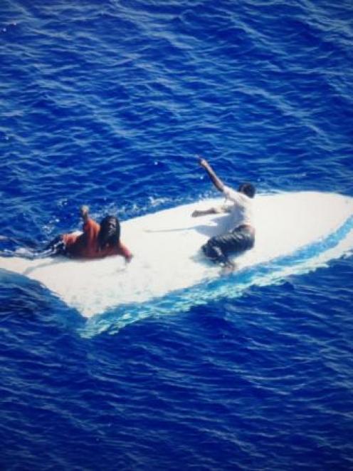 Mike Russell and Anthony Douglas cling to the hull of their capsized vessel as a Coast Guard MH...