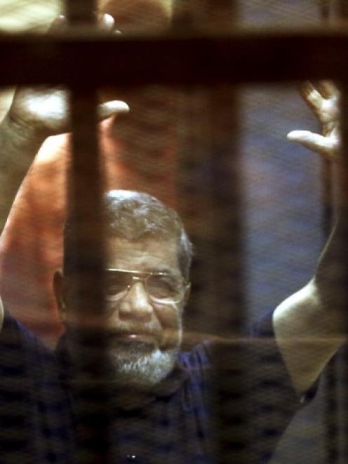 Mohamed Mursi gestures while behind bars at a court in the outskirts of Cairo. Photo Reuters