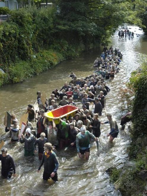 Mud-caked residents of Selwyn College in Dunedin carry a cast-iron bath down the Water of Leith...