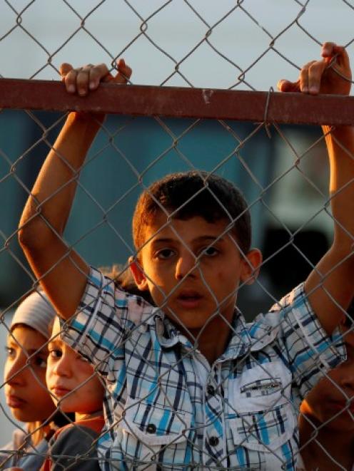 New Syrian refugee children look out from behind a fence as they arrive at a stopover facility...