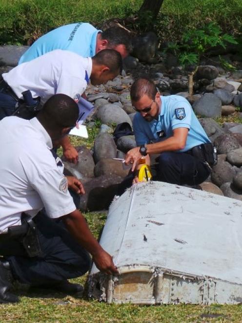 Officials inspect a large piece of plane debris on the beach in Saint-Andre, on the island of La...