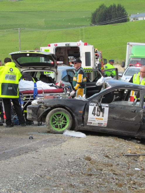 Paramedics (left) treat the driver beside his crashed car where it came to rest after hitting a...