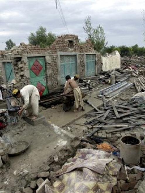 Pakistani villagers collect their belongings amid the rubble of their houses which collapsed in...