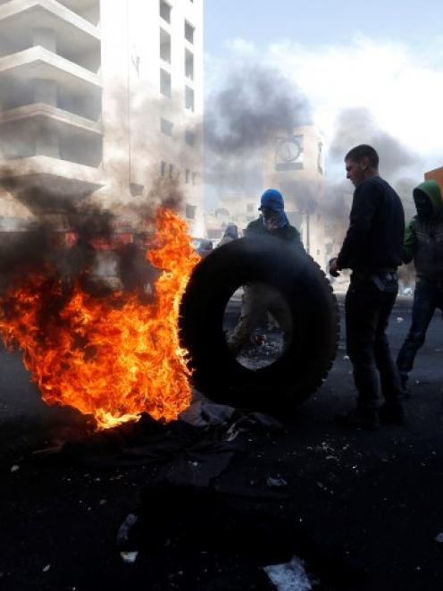 Palestinian protesters stand next to a burning tyre during clashes with Israeli troops in the...