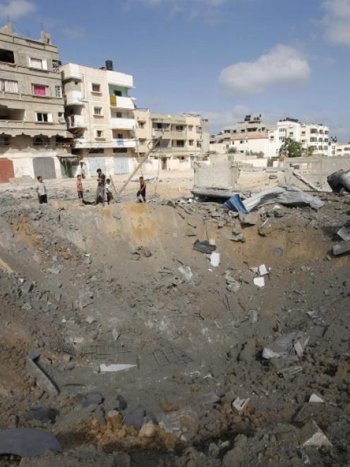 Palestinians stand next to a crater which police said was caused by an Israeli air strike in Gaza...
