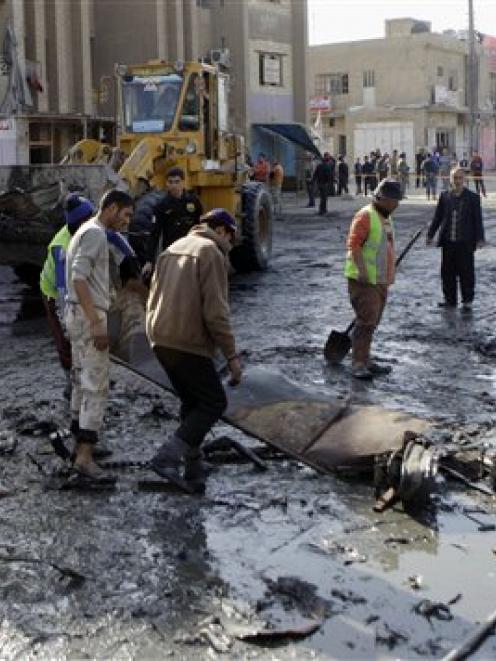 People clean the scene of a car bomb attack in Zafaraniyah, Baghdad, in which 33 people were...