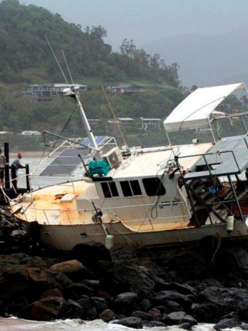 People look at a boat that was washed up on to rocks at Airlie Beach about 120km southeast of...