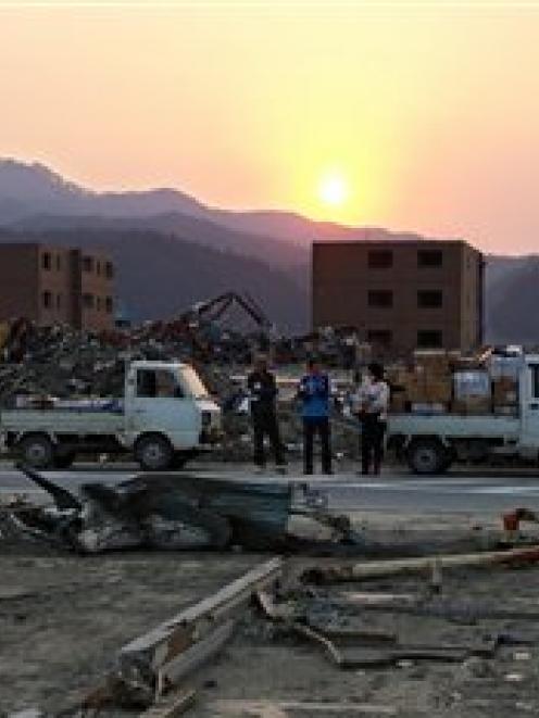 People stand among the rubble in the area devastated by the Match 11 earthquake and tsunami in...