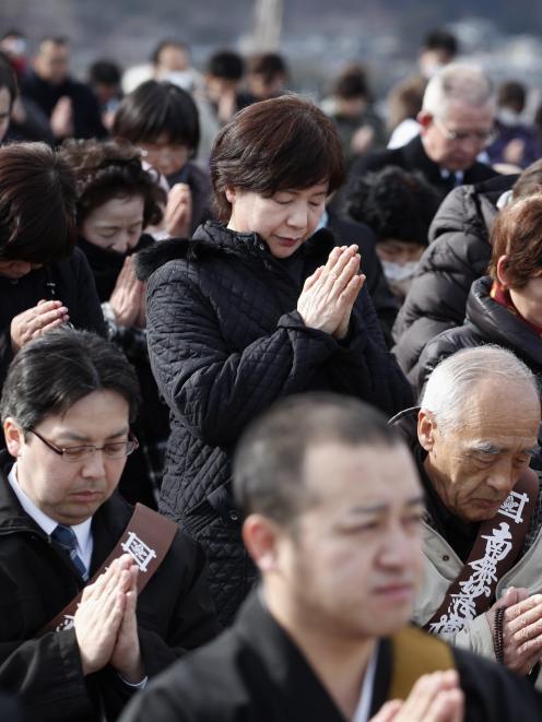 People take part in a moment of silence during a ceremony at an area damaged by the March 11,...